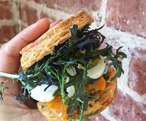 Indulgent buttermilk biscuit egg sandwich with greens, roasted seasonal vegetables, and pasture-raised egg at Standard Fare in Berkeley, CA
